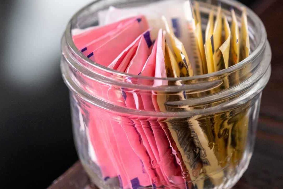 Você usa adoçante de mesa ou adoçante dietético? Imagem com pote contendo saches de adoçantes artificiais para ilustrar artigo de Paty Ayres